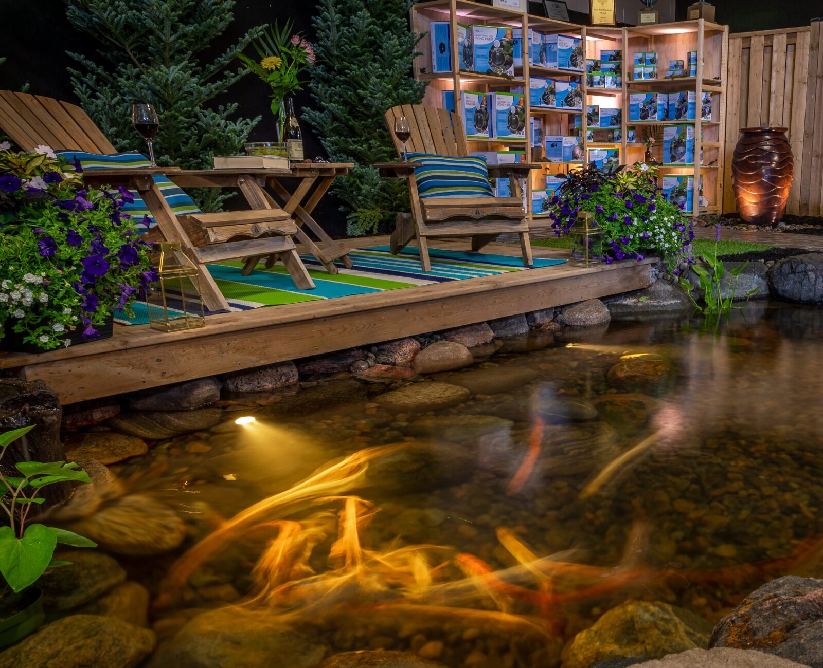 Cozy garden scene with a wooden deck, chairs, koi pond, plants, and decorative lighting, creating a serene outdoor living space.