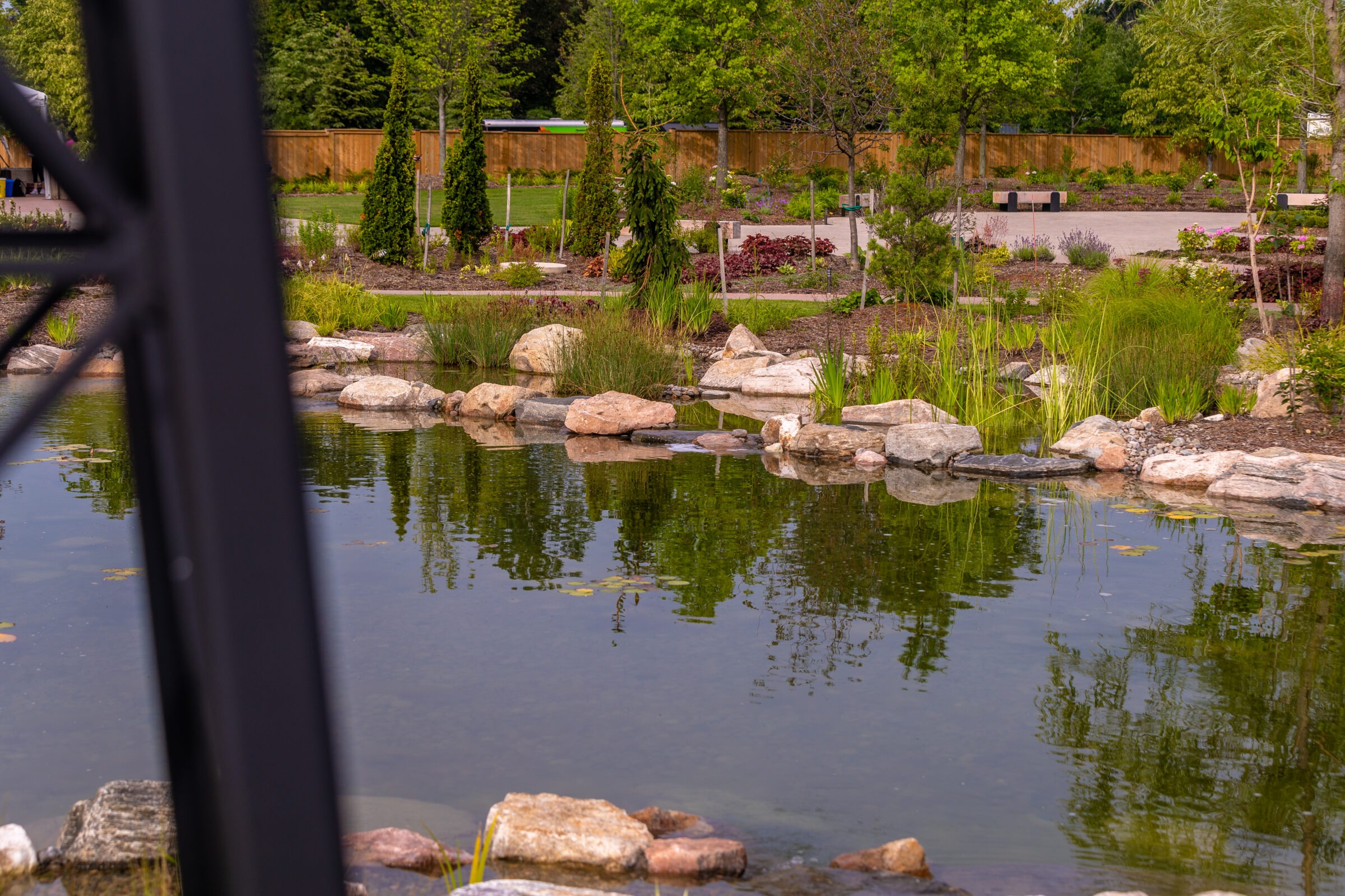 Peaceful park scene with a tranquil pond, surrounded by lush greenery and stone landscaping, creating a serene natural oasis.