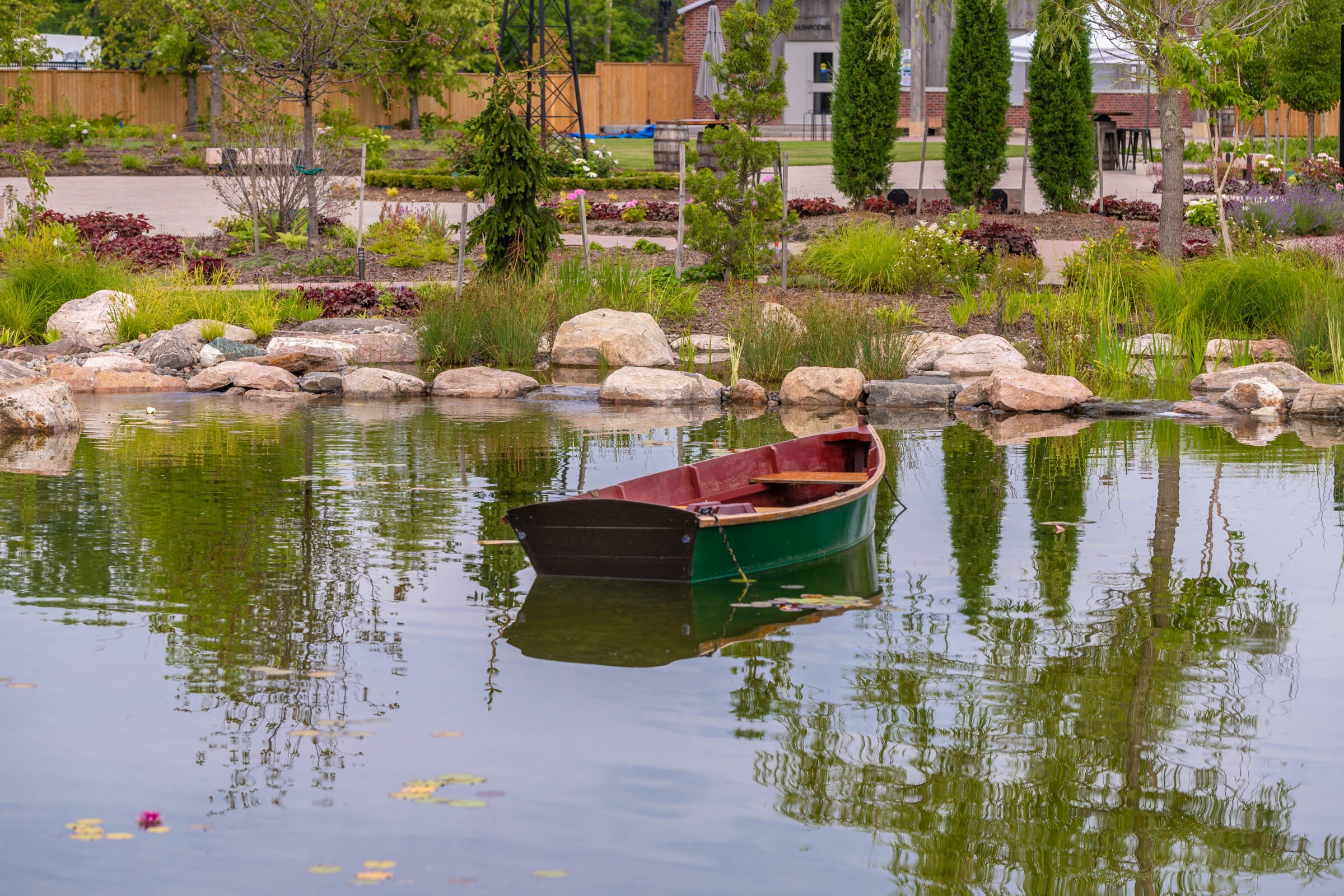A green boat floats in a small, tranquil pond surrounded by rocks and lush greenery, reflecting a peaceful garden scene.