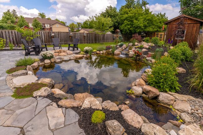 Pond v. pondless waterfalls presented in a picturesque backyard with a large, stone-lined pond.
